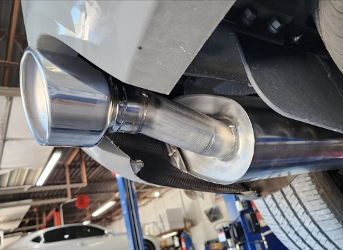 Close-up of a shiny aftermarket car exhaust tip installed on the rear of a vehicle in a workshop.