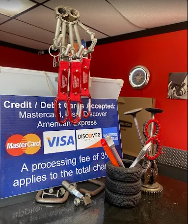 Mechanical hand sculpture made of metal parts hangs above a sign listing accepted credit cards, with metal art and tools on a counter.